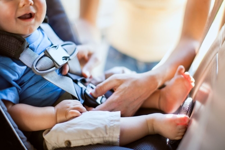 A mom buckles her infant son safely into a rear facing car seat