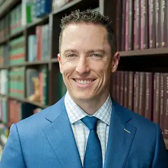 Woodbridge attorney headshot in a blue suit with law shelves in background, representing Gregory G.